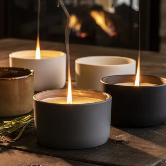 Collection of lit ceramic candle vessels in warm tones on a wooden surface by a fireplace