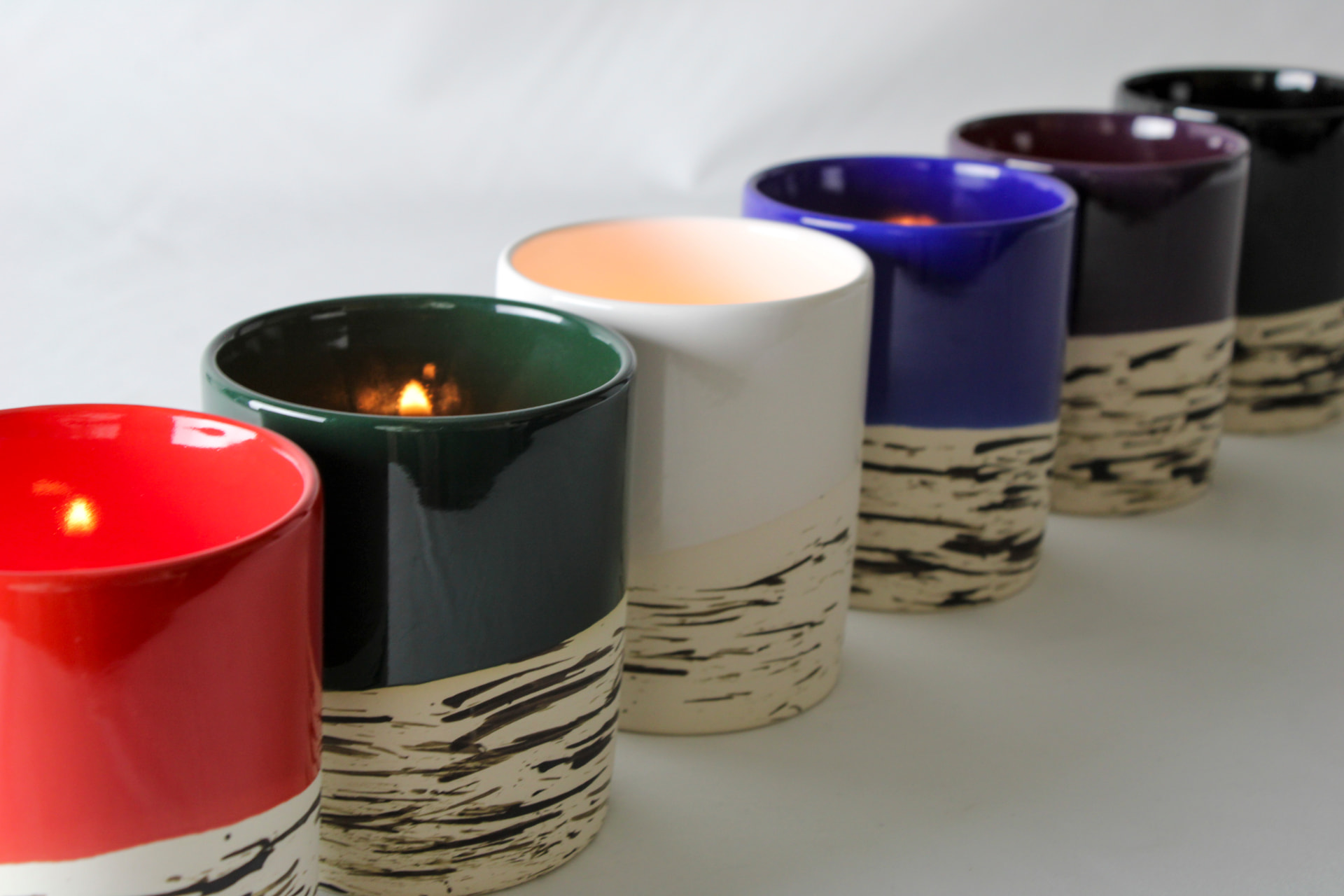 Row of colorful ceramic candle vessels with birch-bark patterned bases